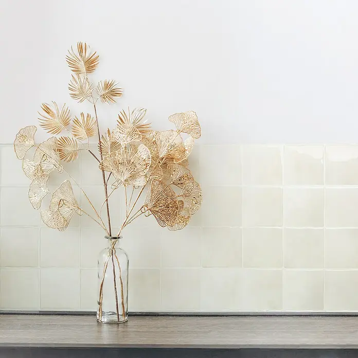 Smart Tiles Selbstklebemosaik Zellige - 22,86 x 22,86 cm, Oia, Glänzend - Goldene Deko-Zweig mit filigranen Blättern in einer Glasvase auf einer dunklen Oberfläche, die einen Hauch von Eleganz und Stil in jeden Raum bringt.