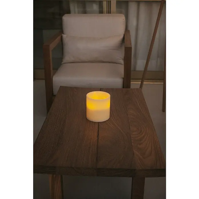 New Garden Lámpara de sobremesa LED redonda Vela Dolo - 0,18 W, Ø x Al: 15 x 15 cm, Blanco, Blanco cálido - Vela decorativa LED sobre mesa de madera rústica con silla al fondo, creando un ambiente acogedor.