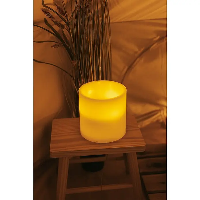 New Garden Lámpara de sobremesa LED redonda Vela Dolo - 0,18 W, Ø x Al: 15 x 15 cm, Blanco, Blanco cálido - Primer plano de una vela LED sobre un taburete de madera pequeño, que emite una luz cálida y amarilla. Elemento decorativo para un ambiente acogedor.