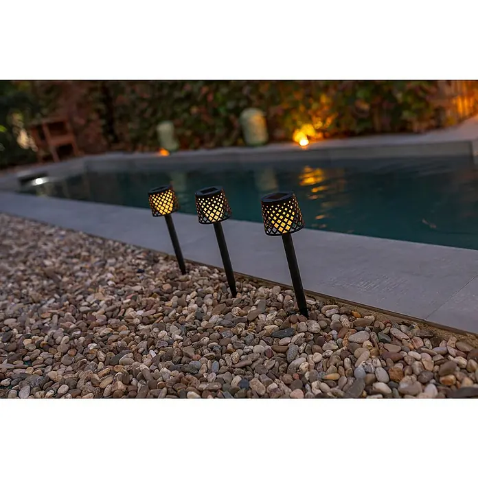 New Garden Estaca solar Gretita - L x An x Al: 7 x 7 x 39 cm, Negro, 4 lm - Primer plano de tres antorchas solares que bordean una piscina, emitiendo una luz cálida y creando un ambiente acogedor.