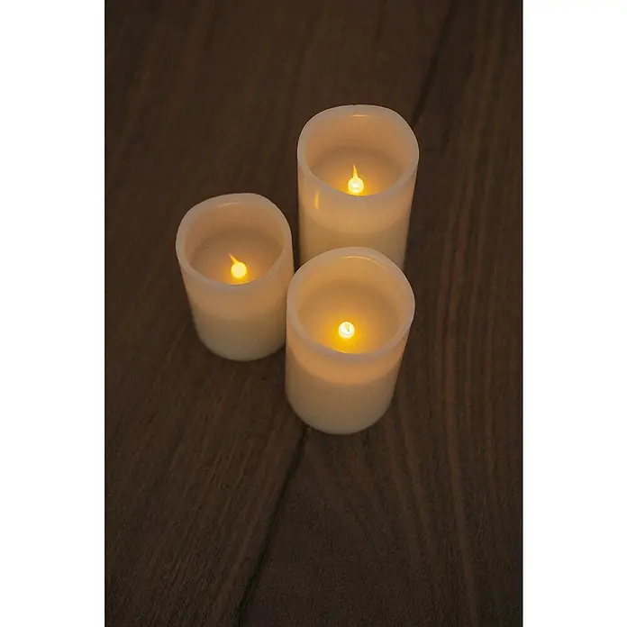 New Garden Lámpara de sobremesa LED redonda Vela Dolo - 0,54 W, Ø x Al: 15 x 15 cm, Blanco, Blanco cálido, 3 ud. - Tres velas LED de diferentes tamaños dispuestas sobre una mesa de madera oscura, sus luces cálidas crean un ambiente acogedor.