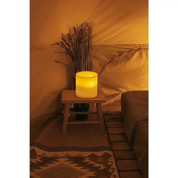 New Garden Lámpara de sobremesa LED redonda Vela Dolo - 0,18 W, Ø x Al: 15 x 15 cm, Blanco, Blanco cálido - Una escena acogedora con una vela brillante sobre un taburete, rodeada de un ambiente cálido.