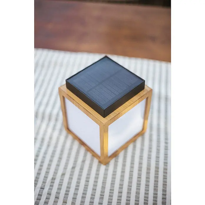 New Garden Lámpara decorativa solar Vega - Blanco cálido, Marrón, LED, IP44 - Primer plano de una lámpara solar en forma de cubo con marco de madera y un panel solar en la parte superior, sobre un paño a rayas.