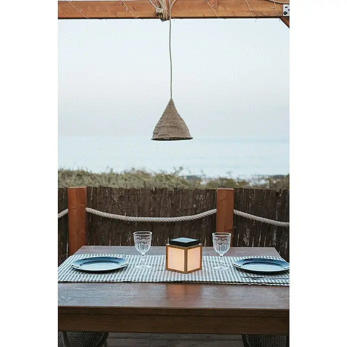 New Garden Lámpara decorativa solar Vega - Blanco cálido, Marrón, LED, IP44 - Mesa puesta con platos, vasos y un farolillo. Una lámpara cuelga encima, con vistas al mar al fondo.