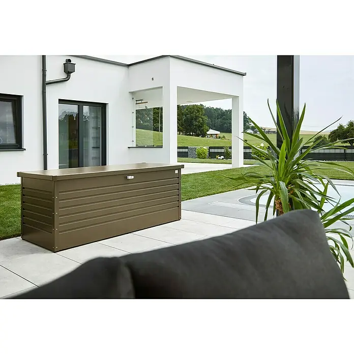 Biohort FreizeitBox Gartenbox 180 - L x B x H: 181 x 79 x 71 cm, Bronze-Metallic, Stahl - Eine braune Biohort-Aufbewahrungsbox steht auf einer Terrasse vor einem modernen Haus. Sie bietet Stauraum für Gartenutensilien.