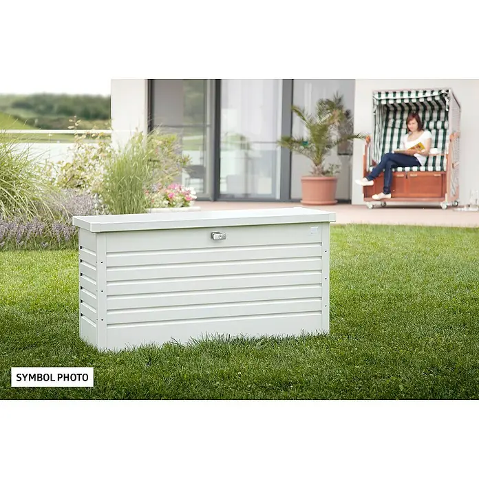 Biohort FreizeitBox Gartenbox 100 - L x B x H: 101 x 46 x 61 cm, Weiß, Stahl - Eine weiße Gartenbox steht auf einem Rasen. Im Hintergrund sitzt eine Frau in einem Strandkorb.
