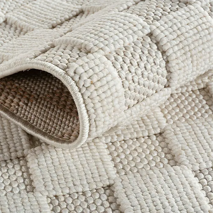 Flachgewebeteppich Helix 2203 - Creme, 340 x 240 cm, 100 % Polyester - Detailansicht eines gerollten, quadratisch gemusterten Teppichs in sanften Naturtönen, der Textur und Handwerkskunst betont.