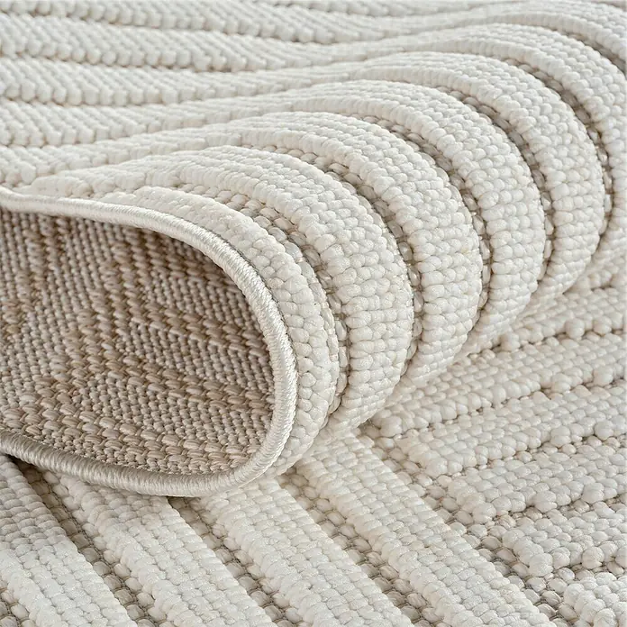 Flachgewebeteppich Helix 2201 - Creme, 110 x 60 cm, 100 % Polyester - Nahaufnahme eines gerollten, cremefarbenen Teppichs mit strukturierter Oberfläche, der Komfort und Qualität ausstrahlt.