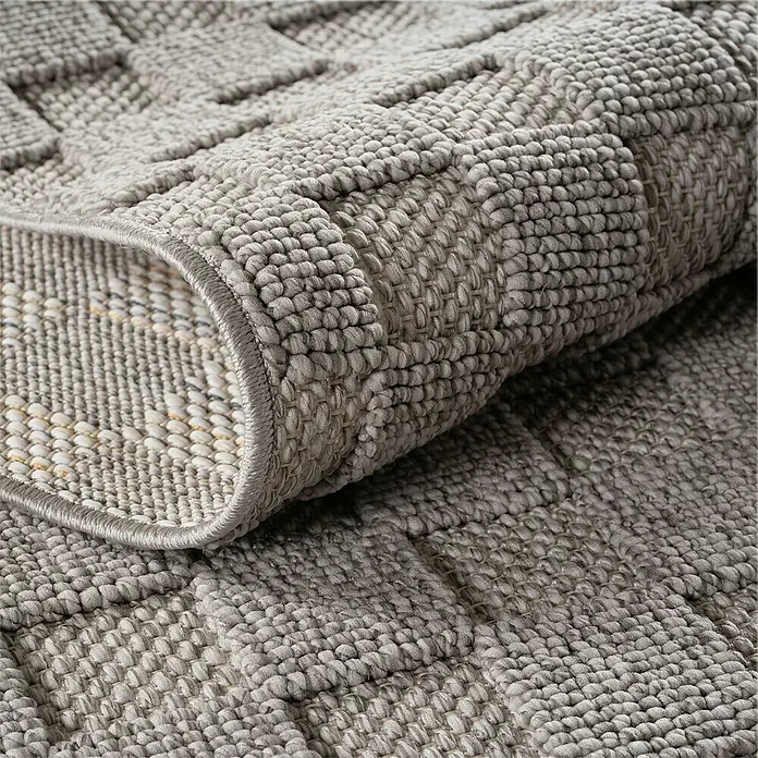 Flachgewebeteppich Helix 2203 - Silber, Durchmesser: 200 cm, 100 % Polyester - Nahaufnahme eines grauen Teppichs mit strukturiertem Muster und aufgerolltem Rand, der die Unterseite zeigt.