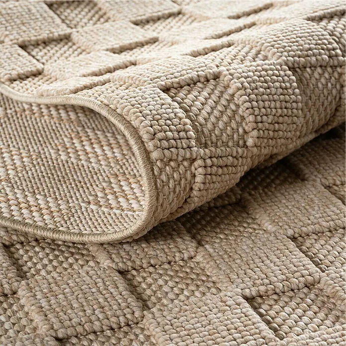 Flachgewebeteppich Helix 2203 - Beige, 340 x 240 cm, 100 % Polyester - Nahaufnahme eines beigen Teppichs mit gewebtem Muster, der teilweise aufgerollt ist, um seine Textur zu zeigen.
