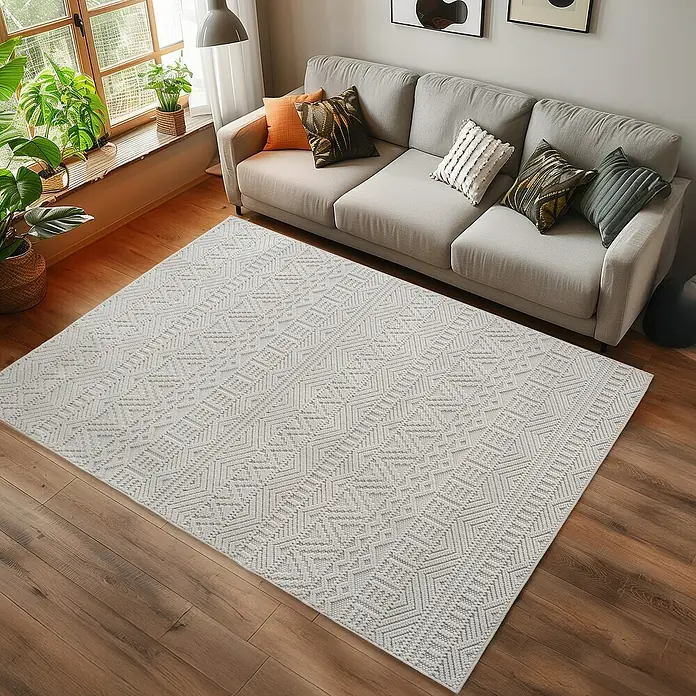 Flachgewebeteppich Helix 2202 - Creme, 370 x 280 cm, 100 % Polyester - Ein rechteckiger Teppich mit einem geometrischen Muster liegt vor einem hellgrauen Sofa auf einem Holzboden.