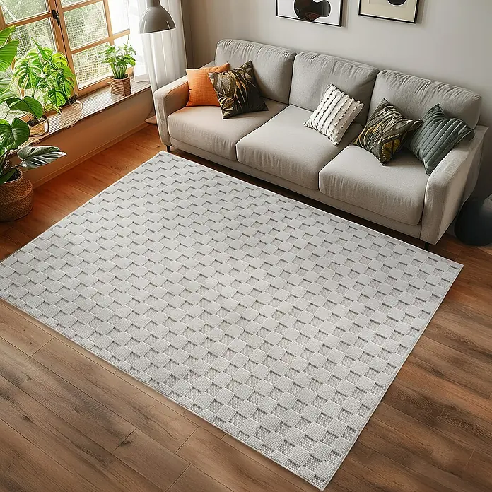 Flachgewebeteppich Helix 2203 - Creme, 340 x 240 cm, 100 % Polyester - Ein grauer Teppich mit einem geometrischen Würfelmuster liegt in einem Wohnzimmer mit einem Sofa und Pflanzen.