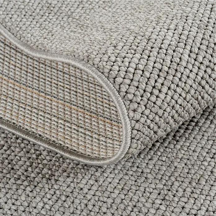 Flachgewebeteppich Helix 2200 - Silber, 170 x 120 cm, 100 % Polyester - Detailaufnahme eines grauen Teppichs mit gewebter Textur und umgeschlagener Ecke, die die Unterseite zeigt.