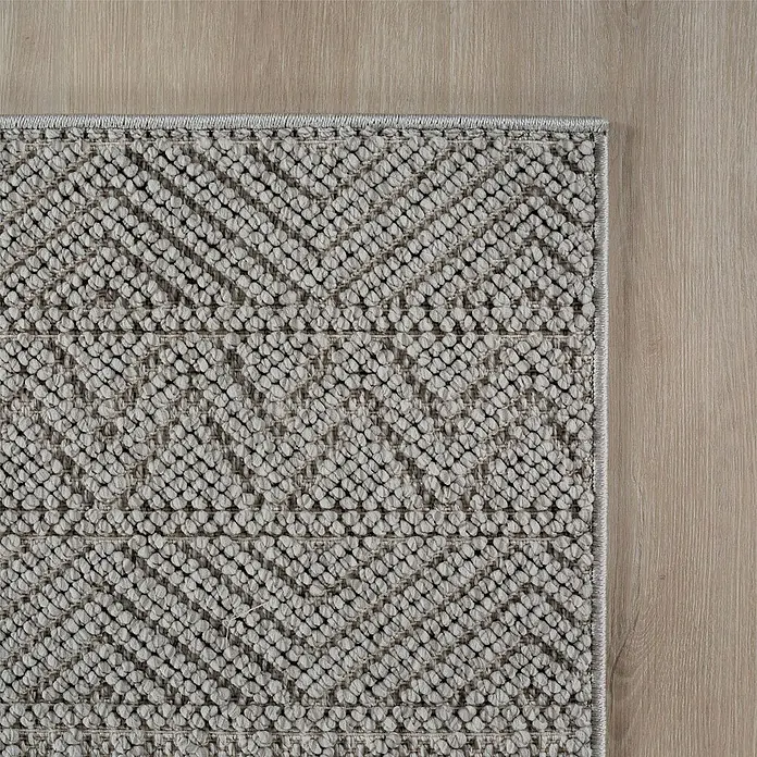 Flachgewebeteppich Helix 2202 - Silber, Durchmesser: 120 cm, 100 % Polyester - Nahaufnahme eines grauen Teppichs mit geometrischem Muster auf einem Holzboden. Der Teppich hat eine getuftete Textur.