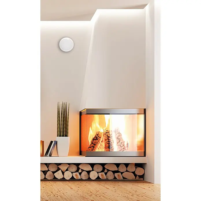 Heizspar-Set - Durchmesser: 12,5 cm, Weiß - Nahaufnahme eines eleganten, modernen Kamins mit Brennholz und einem runden, weißen Gerät an der Wand, das für ein stilvolles Ambiente sorgt.