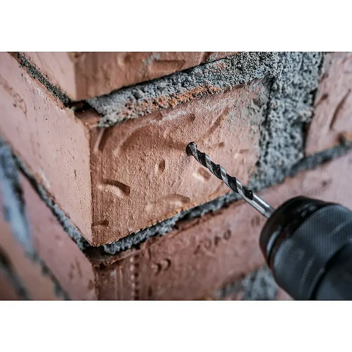 Bosch Broca para hormigón y mampostería HEX-5 - Diámetro de la broca: 3 mm, Longitud de trabajo: 50 mm, Largo: 100 mm - Un albañil perfora un ladrillo con un taladro para hacer fijaciones. La broca es muy visible en la imagen.