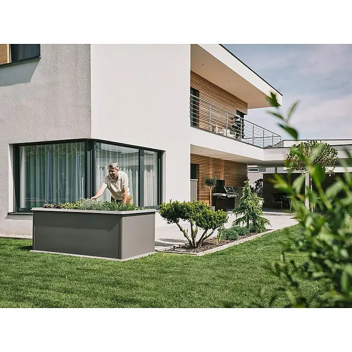 Biohort Hochbeet - 102 x 201 x 77 cm, Stahl, Quarzgrau Metallic - Ein großer, grauer Pflanzkasten aus Metall vor einem modernen Haus mit einem Mann, der sich um die Pflanzen kümmert. Ideal für Garten und Terrasse.