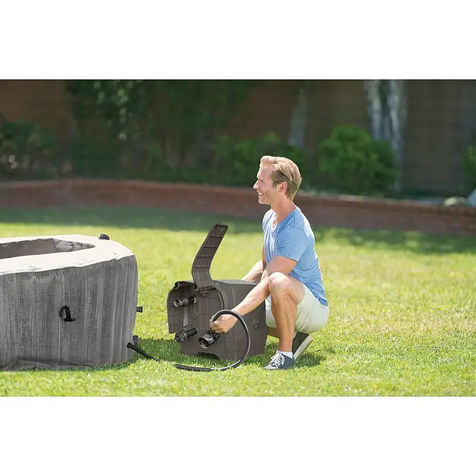 Intex Mobil-Whirlpool Greywood Deluxe Bubble - Ø x H: 216 x 71 cm, Grau, 1.098 l - Ein Mann installiert einen aufblasbaren Whirlpool im Garten, wobei er das dazugehörige Steuerungselement anschließt.