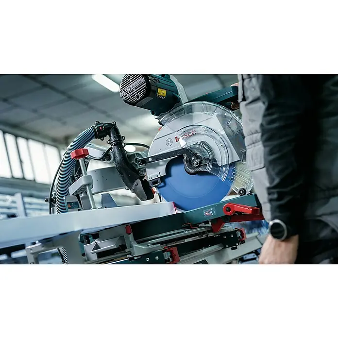 Bosch Expert Kreissägeblatt Expert Multi Material - 216 mm, Anzahl Zähne: 64 Stk., Schnittbreite: 2,4 mm - Eine Nahaufnahme einer Bosch Kapp- und Gehrungssäge, die ein Werkstück schneidet, wobei die blaue Klinge und das klare Schutzschild deutlich sichtbar sind.