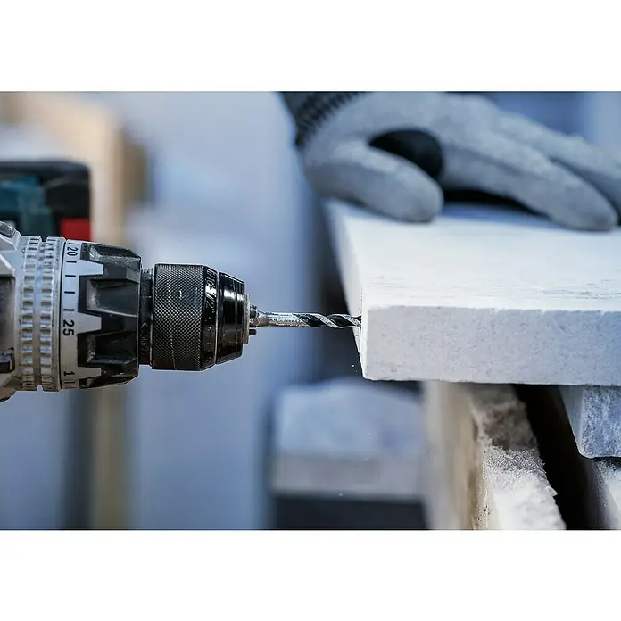 Bosch Broca para hormigón y mampostería HEX-5 - Diámetro de la broca: 12 mm, Longitud de trabajo: 100 mm, Largo: 150 mm - Primer plano de un taladro con una broca haciendo un agujero en un material blanco, mientras una mano enguantada lo sujeta.