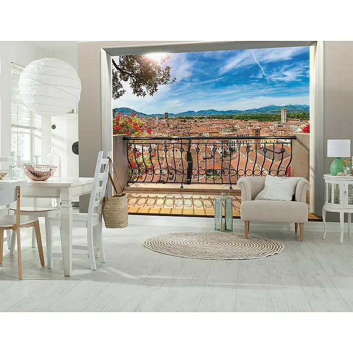 Komar Fototapete Balcony - 4 -tlg., B x H: 368 x 248 cm, Vlies - Helle Inneneinrichtung mit Esstisch, Stuhl, Sessel und einem Ausblick auf eine italienische Stadt, die durch eine Balkonbrüstung begrenzt wird.