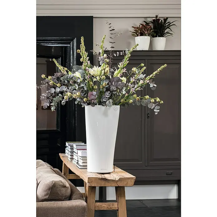 Lechuza Pflanzsäule rund Delta - Kunststoff, Weiß - Ein hoher, weißer Lechuza-Blumentopf auf einem Holztisch, gefüllt mit üppigen Blumen. Elegante Dekoration für ein stilvolles Zuhause.