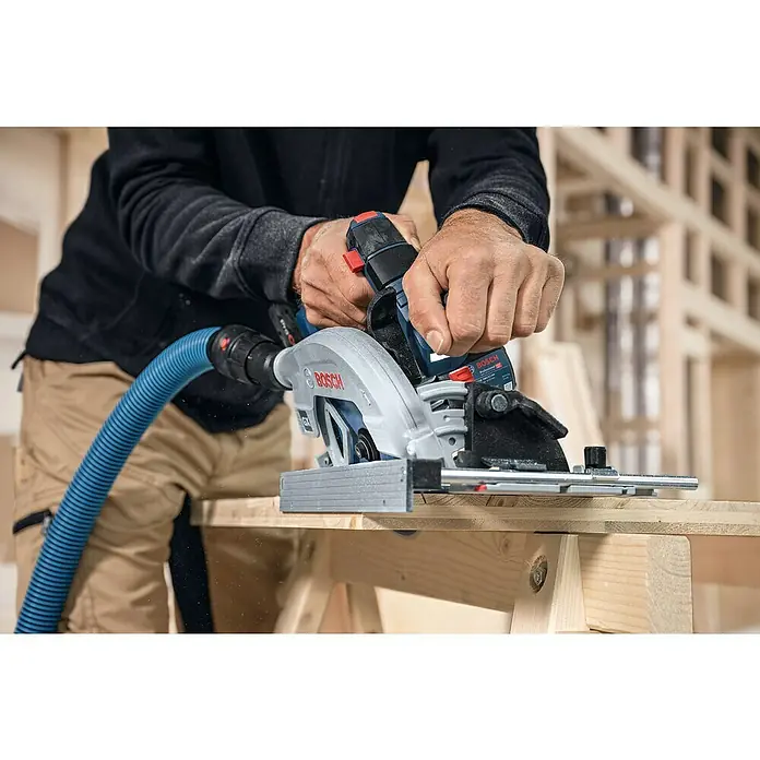 Bosch Professional AMPShare 18V Akku-Handkreissäge Pro Heavy Duty GKS 18V-57-2 GX - 18 V, Ohne Akku, Durchmesser Sägeblatt: 165 mm, 5.000 U/min - Akkubetriebene Handkreissäge Bosch Professional beim Sägen eines Holzbretts. Das Gerät ist mit einem blauen Saugschlauch verbunden.