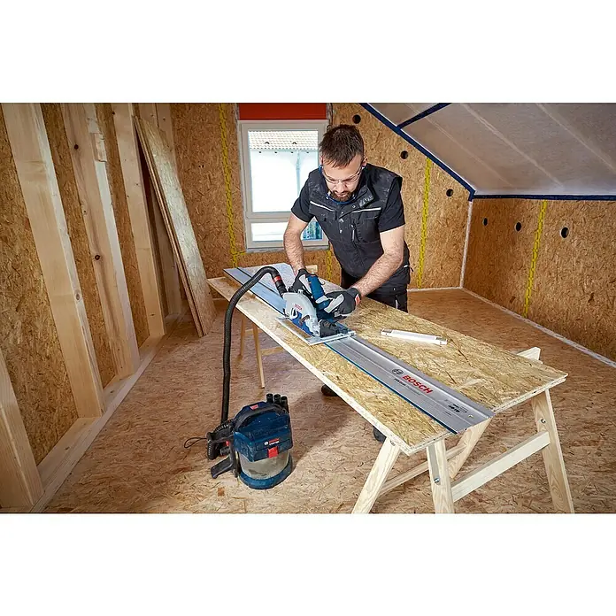 Bosch Professional AMPShare 18V Akku-Handkreissäge Pro GKS18V-68G - 18 V, Ohne Akku, Durchmesser Sägeblatt: 184 mm - 190 mm, 2.500 U/min - 5.000 U/min - Ein Mann sägt mit einer Bosch Tauchsäge auf einem Werkbrett, während ein Staubsauger daneben steht.
