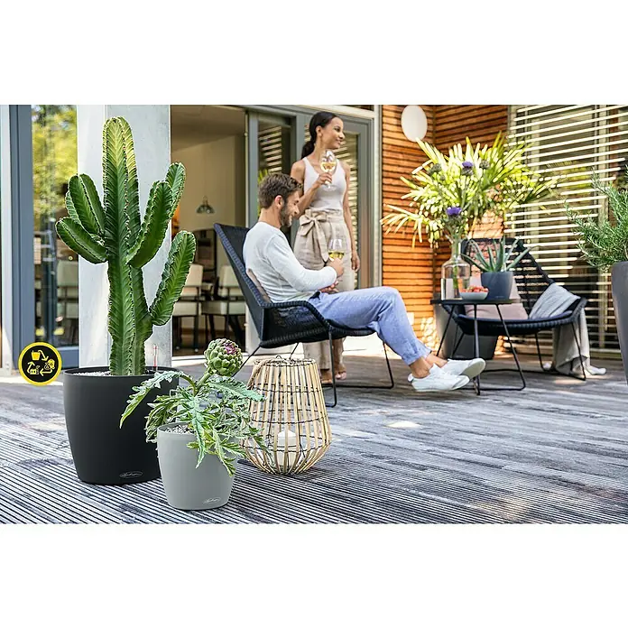 Lechuza Classico Pflanztopf Eco - Außenmaß (Ø x H): 27,5 x 26 cm, Kunststoff, Hellgrau - Schwarze und graue Pflanzgefäße aus Recyclingmaterial mit Recyclingsymbol auf Holzterrasse mit Kakteen und Artischocken.