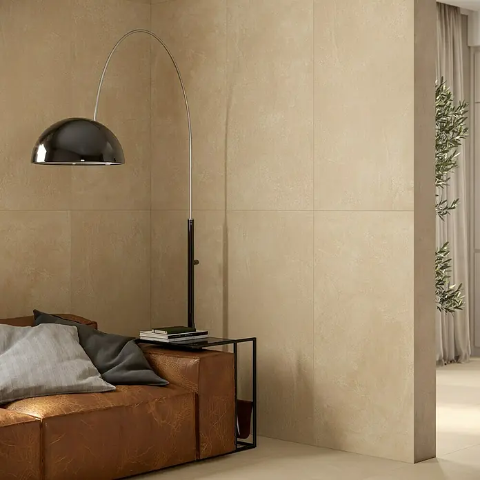 Atlas Concorde Solution Feinsteinzeugfliese Lexington - 60 x 120 cm, Gold, Matt - Große, strukturierte hellbraune Fliesen an Wänden und Boden, gestalten ein modernes Wohnzimmer mit braunem Sofa.