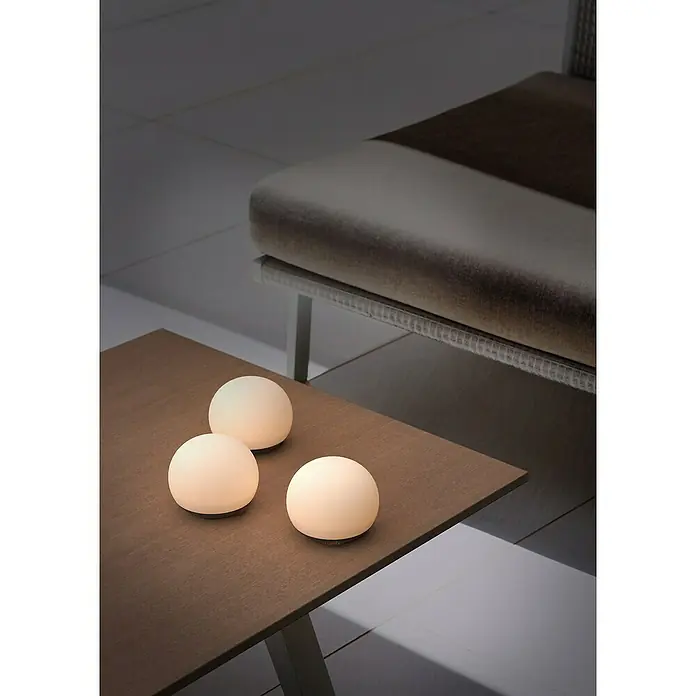 Lumix Solarleuchte Pompom - Lichtfarbe: RGB, Höhe: 100 cm, Pompom - Drei kugelförmige, leuchtende tragbare Lampen stehen auf einem Holztisch und spenden warmes Umgebungslicht.