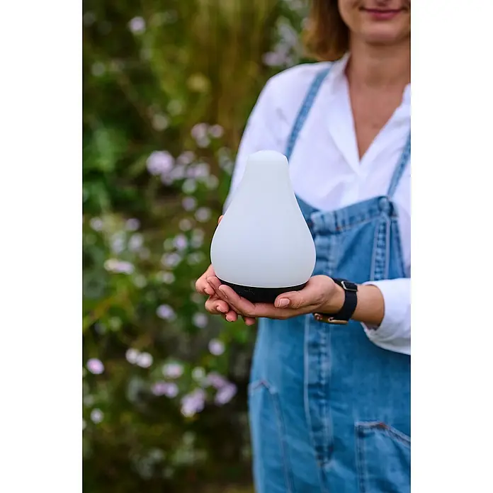 Lumix Solarleuchte Tulip - Lichtfarbe: RGB, Höhe: 100 cm, Tulip - Eine Person hält eine tragbare weiße Laterne mit schwarzem Sockel in den Händen. Die Lampe leuchtet sanft.