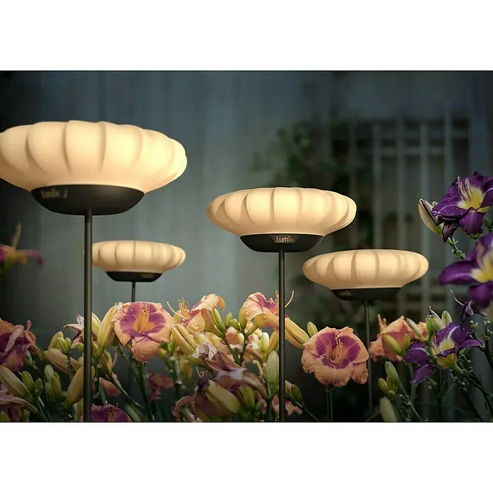 Lumix Solarleuchte Sunny - Lichtfarbe: RGB, Höhe: 100 cm, Sunny - Lumix Gartenleuchten mit hellbeigen, geriffelten Köpfen und schwarzen Basen, die einen Blumengarten beleuchten.