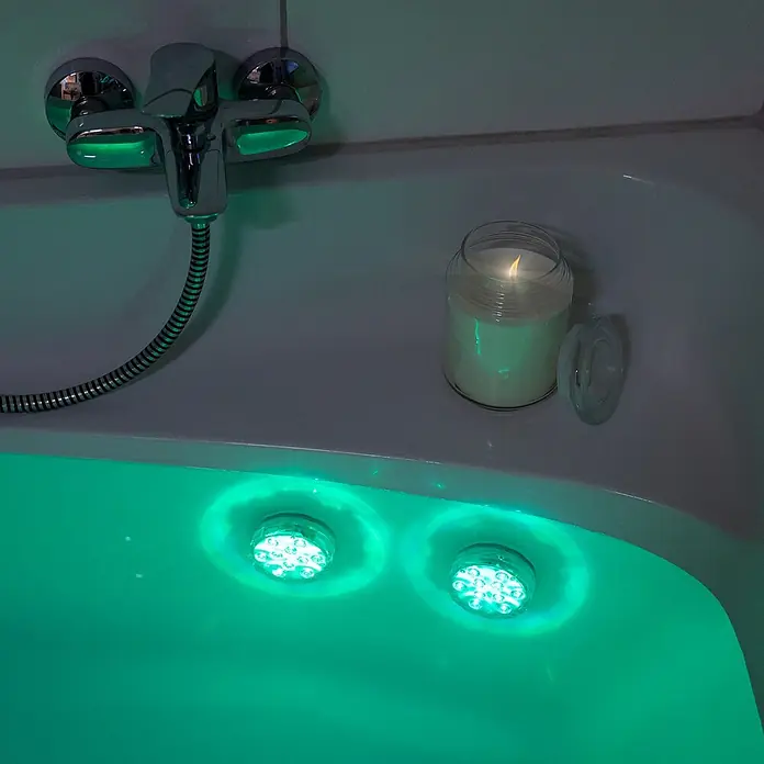 LED-Poolbeleuchtung - Durchmesser: 7 cm, Transparent, LED, RGB - Weiße Badewanne mit zwei grünen LED-Unterwasserleuchten und einer brennenden Kerze am Wannenrand, die eine Spa-ähnliche Atmosphäre schafft.