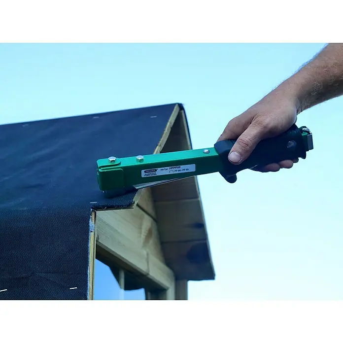 Prebena Hefthammer - Passend für: Prebena Heftklammern der Type PF 6 - 9 mm - Grüner Hammertacker wird von einer Hand zum Befestigen von schwarzem Dachmaterial auf einer Holzkonstruktion verwendet.