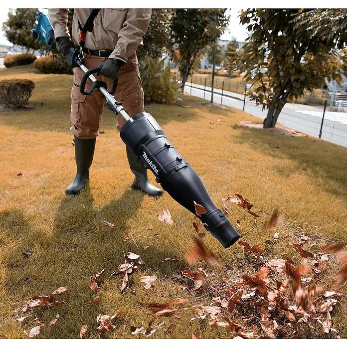Makita Gebläseaufsatz UB401MP - Passend für: DUX18, DUX60, UX01G - Eine Person in Khaki-Kleidung verwendet einen schwarzen Makita Laubbläser, um braune Blätter von einem Rasen zu entfernen.