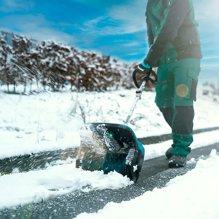 Makita Multifunktionswerkzeug-Zubehör Schneefräsen-Aufsatz SN400MP - Passend für: DUX18, DUX60, UX01G - Person räumt Schnee von einem Weg mit einer teal-schwarzen Makita Akku-Schneeschaufel.