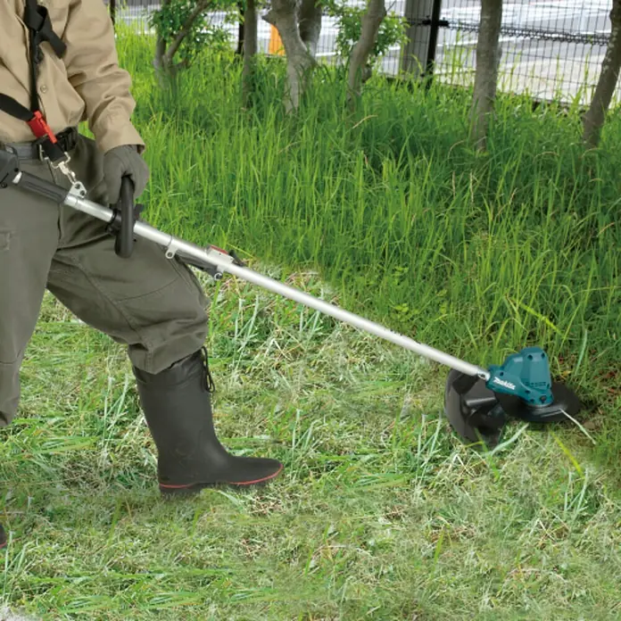 Makita LXT 18V Akku-Rasentrimmer DUR191LZX9 - 18 V, Li-Ionen, Ohne Akku, Schnittbreite Faden: 230 mm - Eine Person verwendet einen türkis-silbernen Rasentrimmer, um hohes Gras im Freien zu schneiden.