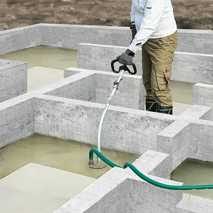 Makita Tauchpumpen-Anschlussstück PF400MP - Passend für: DUX18, DUX60, UX01G - Person bedient eine silberne Handpumpe mit grünem Schlauch, um schlammiges Wasser aus einem Betonfundament abzuleiten.
