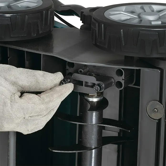 Makita LXT 18V Akku-Vertikutierer DUV320Z - Anzahl Akkus: Ohne Akku, 18 V, Arbeitsbreite: 32 cm - Behandschuhte Hand stellt die Tiefeneinstellung eines schwarzen Gartenlüfters ein, zeigt Spiralzinken und Räder.
