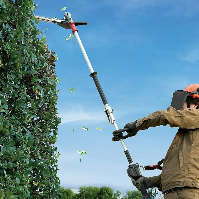 Makita Heckenscheren-Aufsatz EN402MP - Passend für: DUX18, DUX60, UX01G - Eine Person trimmt eine hohe Hecke mit einer grauen und schwarzen Teleskop-Heckenschere.