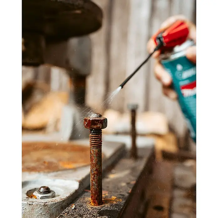 Makita Pflegespray - 0,3 l - Eine Hand sprüht Rostlöser aus einer Dose auf eine stark korrodierte Schraube.