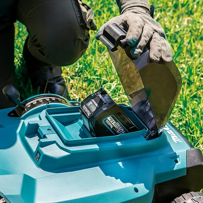Makita XGT 40V max. Akku-Rasenmäher LM004GZ - 40 V, Ohne Akku, 8 Ah, Schnittbreite: 43 mm - Behandschuhte Hand steckt einen schwarzen Makita 40V Akku in einen türkisfarbenen Mähroboter.