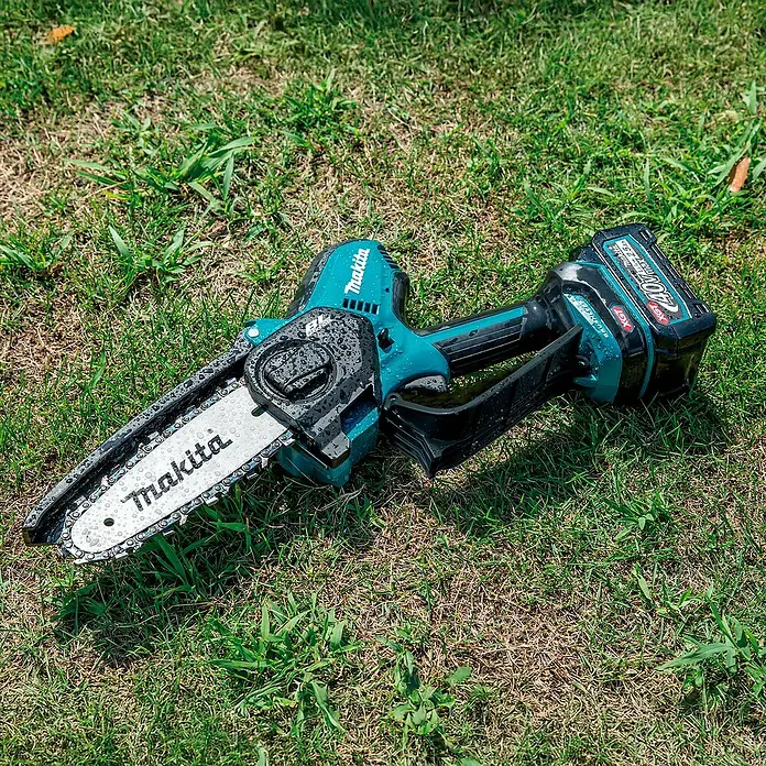 Makita XGT 40V max. Akku-Astsäge UC029GZ - 40 V, Li-Ionen, Ohne Akku, Schwertlänge: 150 mm - Türkis-schwarze Makita Mini-Kettensäge mit 40V Akku, bedeckt mit Wassertropfen.