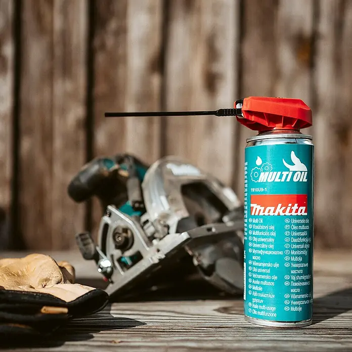 Makita Pflegespray - 0,3 l - Makita Multi-Öl Sprühdose mit rotem Applikator, zur Werkzeugpflege, auf Holz neben Kreissäge und Handschuhen.