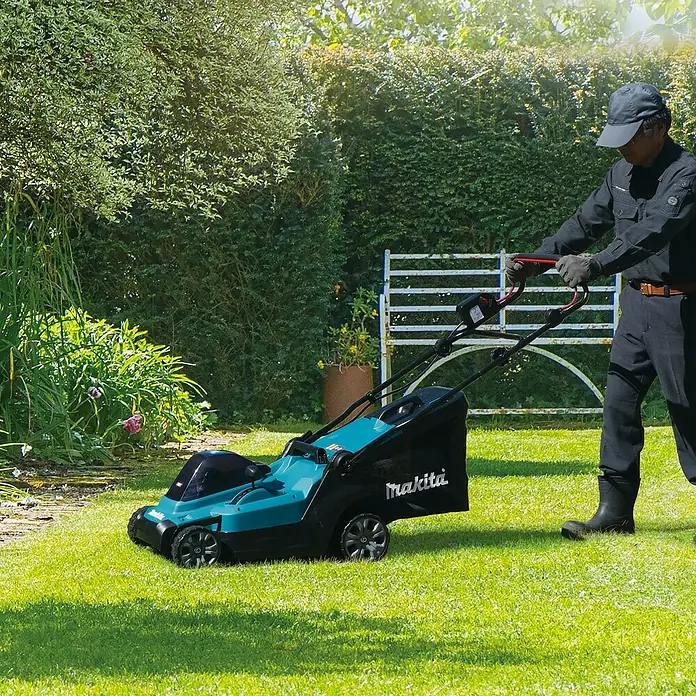 Makita XGT 40V max. Akku-Rasenmäher LM003GZ - 40 V, Ohne Akku, 8 Ah, Schnittbreite: 38 mm - Ein Mann mäht mit einem türkis-schwarzen Makita Rasenmäher Gras in einem sonnigen Garten.