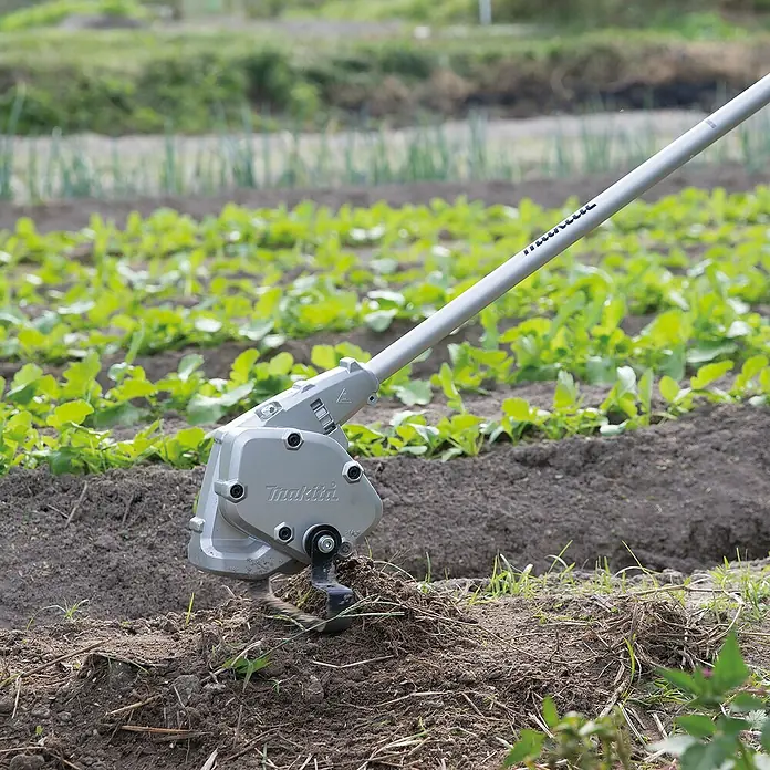 Makita Stahlrad für Motorhacke WA400MP - Passend für: DUX18, DUX60, UX01G - Heller Makita Kultivator-Aufsatz bearbeitet Erde in einem Gartenbeet mit Pflanzen.