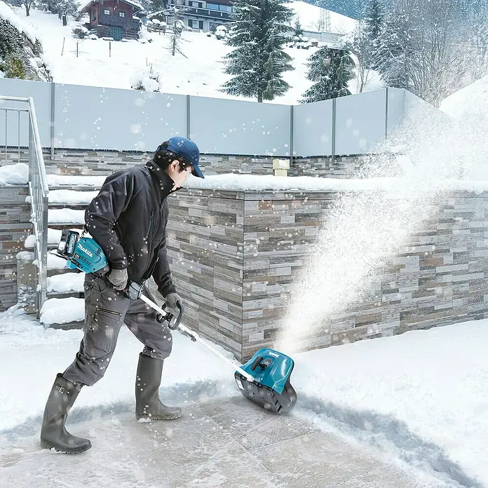 Makita Multifunktionswerkzeug-Zubehör Schneefräsen-Aufsatz SN400MP - Passend für: DUX18, DUX60, UX01G - Eine Person nutzt eine türkis-schwarze Akku-Schneeschaufel, um Schnee von einem Weg zu räumen, wobei Schnee zur Seite geworfen wird.