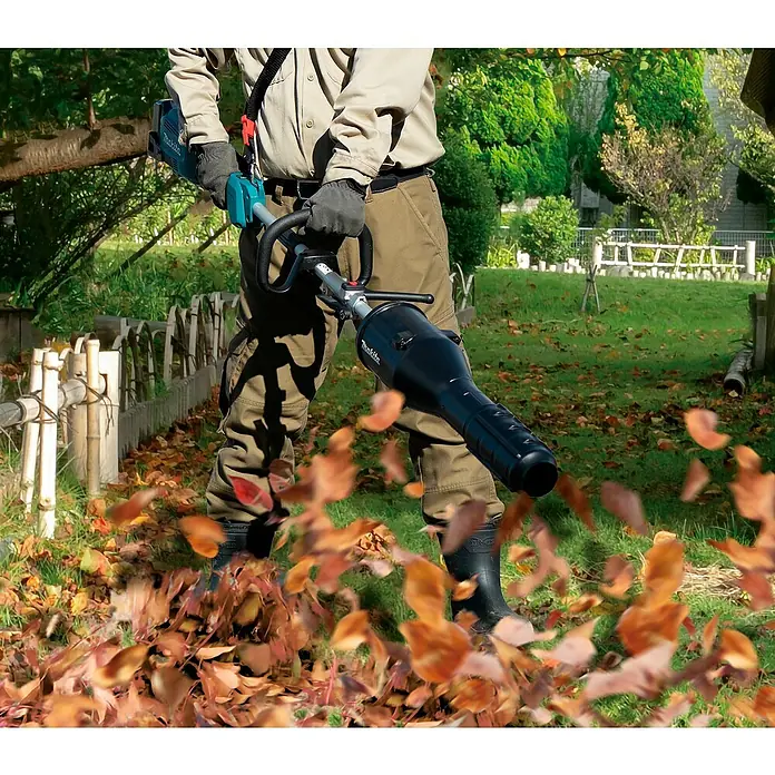 Makita Gebläseaufsatz UB402MP - Passend für: DUX18, DUX60, UX01G - Eine Person nutzt einen schwarz-türkisen Makita Laubbläser, um Herbstlaub im Garten zu entfernen.