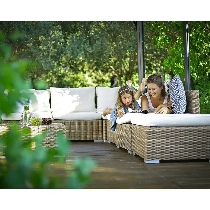 Palram – Canopia Pavillon Milano 4300 - B x T: 435,9 x 315,5 cm, Farbe Gestell: Anthrazit, Aluminium - Zwei Personen entspannen auf einem hellbraunen Rattan-Gartenlounge-Set mit weißen Kissen.